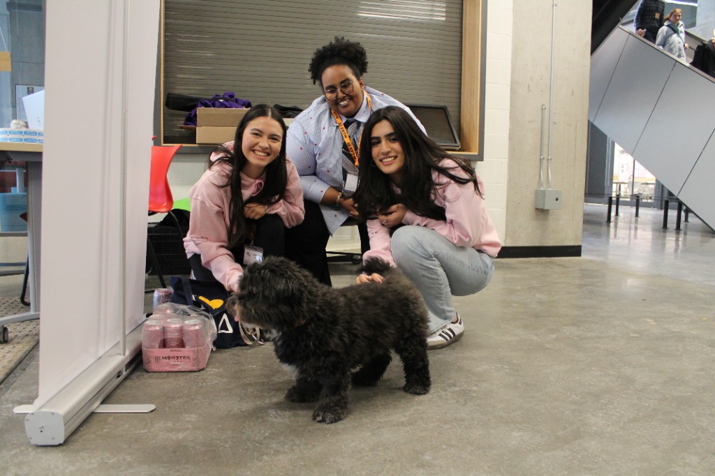 Three students posing indoors with a small dog