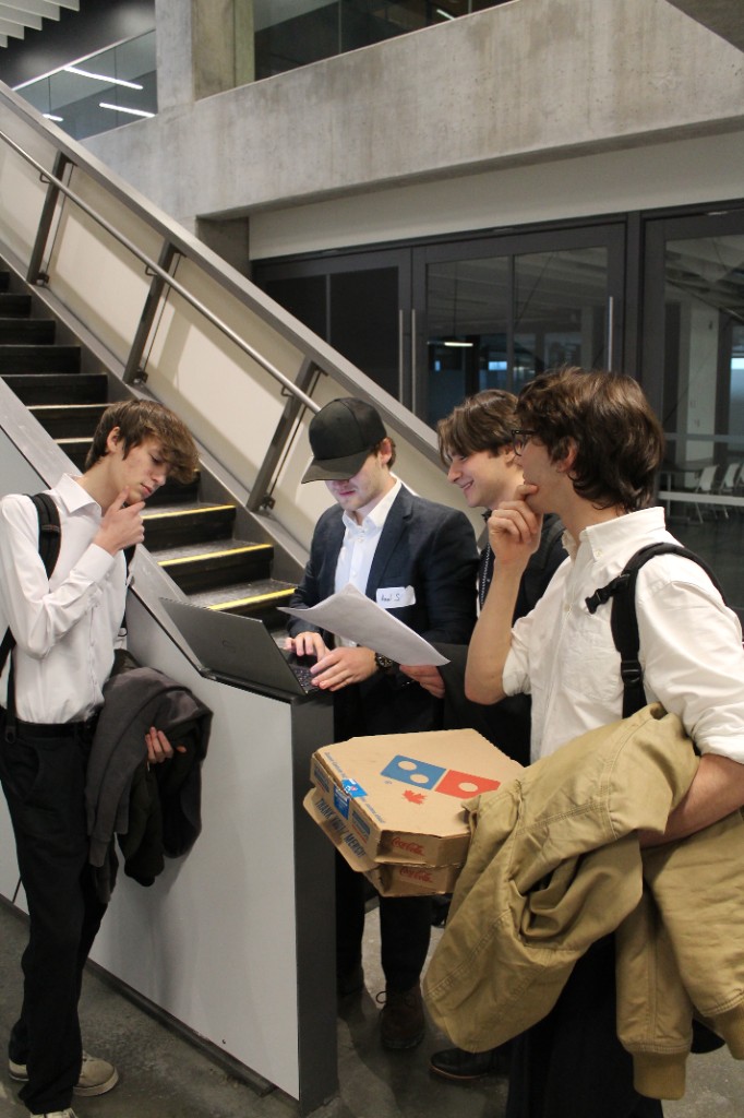 Four students huddled around a laptop in a campus stairwell